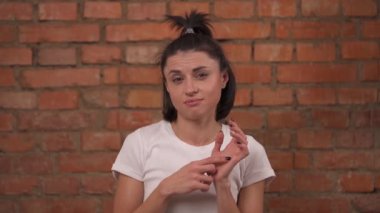 A young thoughtful and skeptical woman stands on brick wall background and flirts on the camera