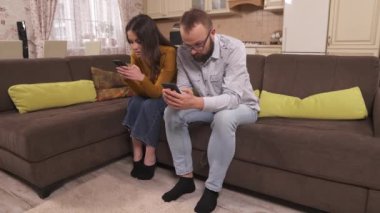 Genç bir esmer ve gözlüklü sakallı bir adam stüdyo dairesinin köşesindeki kanepede oturuyorlar ve ellerinde telefonlar var. Yazıyor ve bir şeyler söylüyor. Ekrana bakıyor ve kaydırıyor.