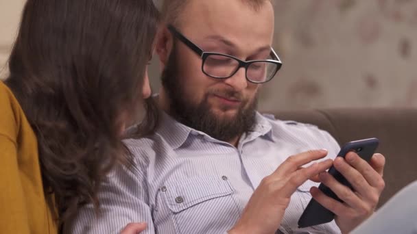 Young Couple Brunette Bearded Man Glasses Sitting Couch Looking Phone — 图库视频影像