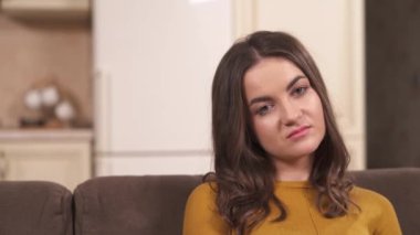 A close-up of brunette's face staring in front of her, the camera moves to the left and there is a closeup of a bearded man's face in glasses sitting and gazing into space