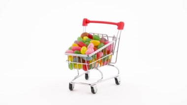Shopping cart filled with vivid jelly candy beans rotating on the turntable. Isolated on the white background. Close-up.