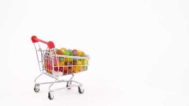 Shopping cart filled with vivid jelly candy beans is moving forward. Isolated on the white background. Close-up. Macro.