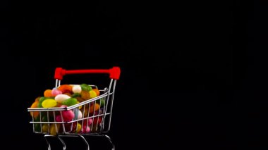 Half frame. Macro shooting of shopping cart filled with vivid jelly candy beans rotating on the turntable. Isolated on the black background.