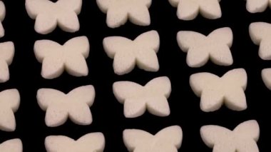 Small butterfly shaped white candies rotating. Isolated on the black background.