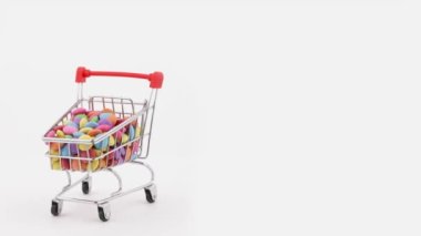 Half frame. Shopping cart filled with colorful sweet chocolate candies rotating on the turntable. Isolated on the white background.