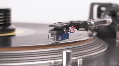 Close-up of LP turntable playing a vinyl. Cuing lamp, clamp, tone arm and coil cartridge atre on the foreground.