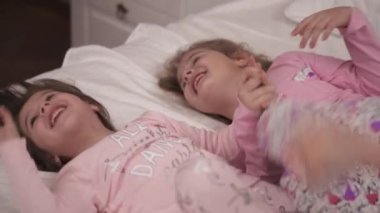 Sevimli küçük kızlar yatakta uzanıyorlar, gülüyorlar ve sarılıyorlar.