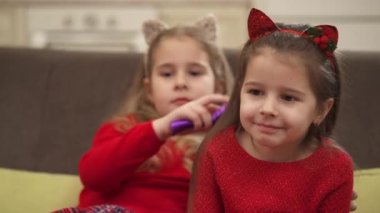 Cute curly girl with a kitten ears headband combing her friends hair