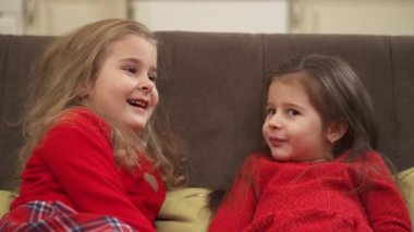 Close up view of a small cute girls in red clothes sitting on the sofa at home and playing with each other.