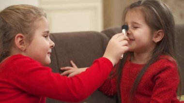 Little girl playing with a makeup brush and tickling her friends nose with it