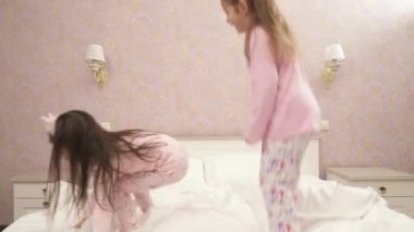 Little cute girls jumping on the bed in pink pajamas