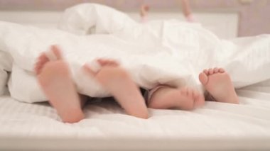 Two pairs of little girls feet in bed under the blanket. Kids having fun in bed.