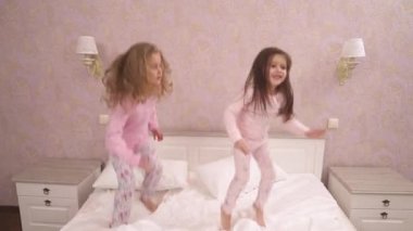 Two little girls in pajamas jumping and dancing on the bed