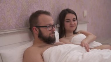 Young couple having problems in bed, a girl lifts a blanket and looks with disappointment at her boyfriend