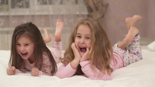 Szczęśliwe Dziewczynki Piżamie Leżą Brzuchu Łóżku Poruszając Skrzyżowanymi Nogami Śmiejąc — Wideo stockowe