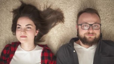 A top view of a happy young couple lying on the floor, looking at the camera and smiling