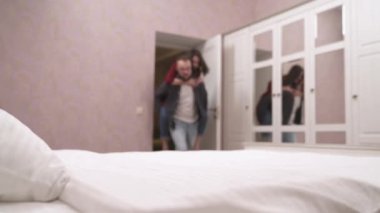 Genç kız erkek arkadaşıyla eğleniyor. Adam kızı sırtında tutuyor ve yatağa atıyor ve öpüyor.