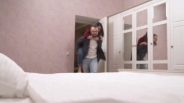 Young girl having fun with her boyfriend. The man holds the girl on his back and then throws her on the bed and kisses