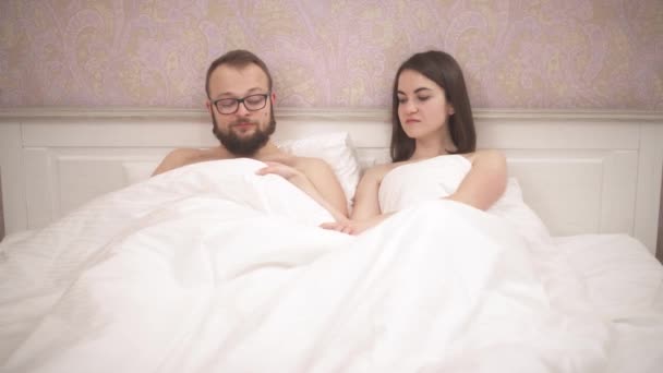 恋人のカップルは ベッドの上に毛布の下に横たわっている 女の子は毛布を持ち上げ 彼女が見たものに驚いて — ストック動画