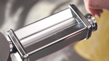 A close-up of dough flatten machine and a hand setting the thickness, and then putting a piece of dough for processing. Fresh noodles preparation in a restaurant