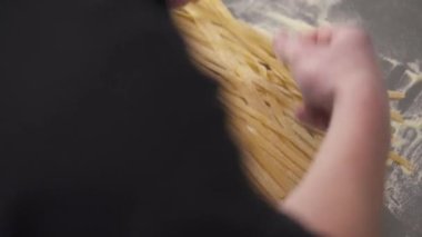 Hands holding a bunch of cut noodles on the table and spreading them on the table with flour. Fresh noodles preparation in a restaurant