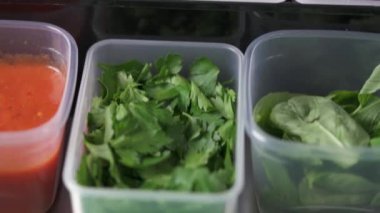 A top view of plastic containers with parsley, spinach, sauce, tomatoes, butter, cherry tomatoes in the professional kitchen