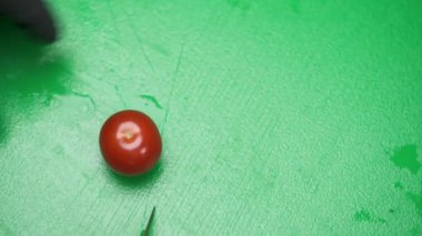 A close-up of green board, hands in black gloves taking cherry tomatoes and cutting them in halves