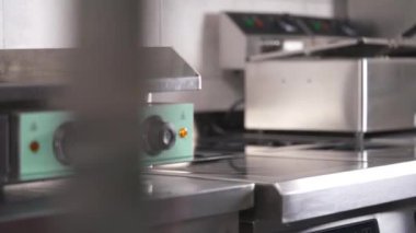 An electric stove panel in the professional kitchen and a hand in black glove puts a frying pan on the stove surface