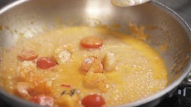 A top view of vegetables and shrimps sizzling in sauce on the frying pan and a hand adds some herbs, salt, mixes it with spoon and leaves it on the stove