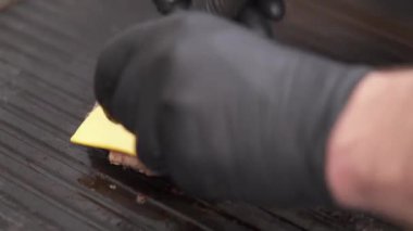 Izgarada kızarmış bir hamburger ve siyah eldivenli bir el üzerine iki kare peynir koyup bir mutfak feneriyle ısıtıyor.