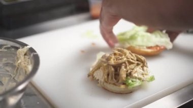 Half of the burger with filling lying on white board on the table and covered with the second toasted half with salad and fixed with a stick in the middle