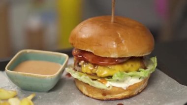 A close-up with burger fixed with a stick, and sauceboat with tomato sauce. The camera moves to the left right and stops at the French fries lying in the corner of the tray