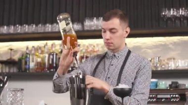 Barın tezgahında duran bir barmen şişeden jigger 'a içki dolduruyor ve sonra da sallanan bardağa.