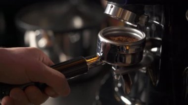 A close-up of a hand holding a portafilter with ground coffee coming out of the electric coffee machine. Coffee making in a bar
