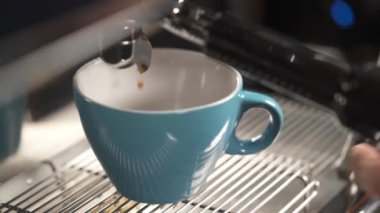 A close-up of light blue cup at the coffee machine and some coffee pouring into it. A hand takes the cup away. Coffee making in a bar