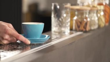 A hand holding a light blue cup on the sauce and putting it on the bar counter. Two hands are taking it away