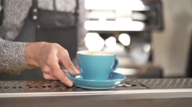 A backside view of a hand holding a light blue cup on the sauce and putting it on the bar counter. Two hands are taking it away