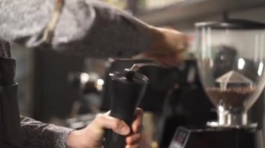 A close-up of hands holding a coffee grinder and winding its handle while grinding coffee beans. Hand brew coffee making