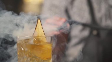 A glass with iced drink with a pear crisp standing on the table and steam starts blowing from behind