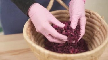 Yakın plan, pembe eldivenli bir kız dikkatlice kurutulmuş gül yapraklarını sıralıyor. Sepet kurumuş çiçeklerle dolu..