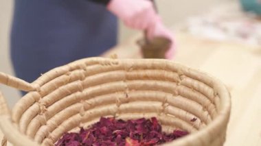 Kurumuş çiçeklerle dolu bir sepete yakından bak. Kamera hareket ediyor ve kızın, kurumuş gül yapraklarını tokmaklı bakır havan topuyla nasıl toz haline getirdiğini gösteriyor..