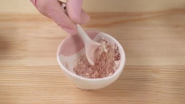 Close-up of a girl mixing powders from different herbs with a spoon in a ceramic bowl.