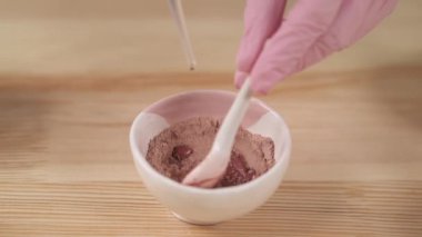 Top view of a girl dripping water in a bowl with herbal powders using a pipette and making natural facial scrub.