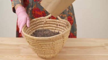 A close-up view of woman's hand holding the paper package and pouring out dried lavender flowers to fill a wicker basket.