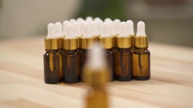 A close-up front view of woman's hand taking small amber bottle with white cap on the blurred background. Arranged bottles go to the foreground.