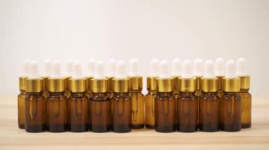 A close-up front view of woman's hand putting small amber bottle with white cap back to the arranged in two lines bottles.