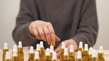 A close-up view of woman choosing small bottle, opening it and rising up to her face. In front of the face she is filling a pipette and holding it above the bottle.