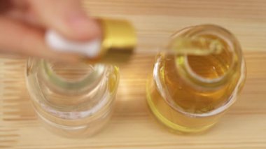 A top view of the pipette filled with oil from the first bottle. The full pipette is put above the second bottle with water and oil droplets are dropping into water.