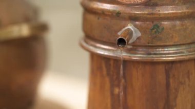 A close-up view of the water drops flowing out of metal jar on a wooden support.