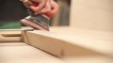 A front view of man's hand holding pneumatic power sander to polish a wooden frame.